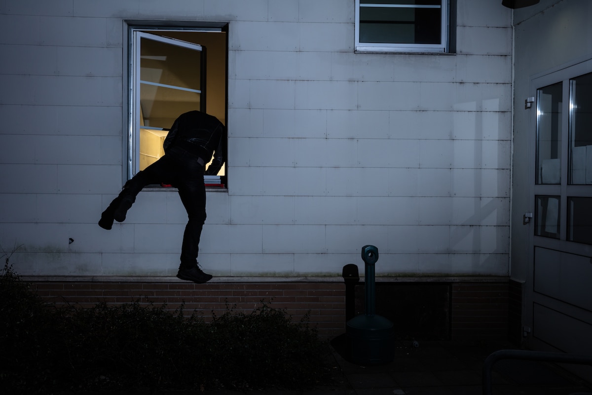 Rear View Of A Burglar Entering In A House Through A Window cambriolage vol habitation fenêtre châssis voleur cambrioleur nuit